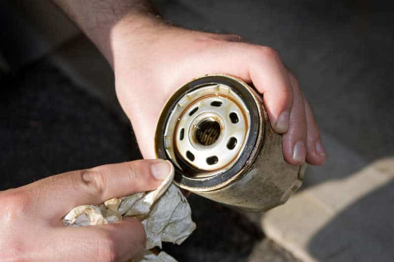 A backyard mechanic wipes the seal of a slightly used oil filter of lawn mower