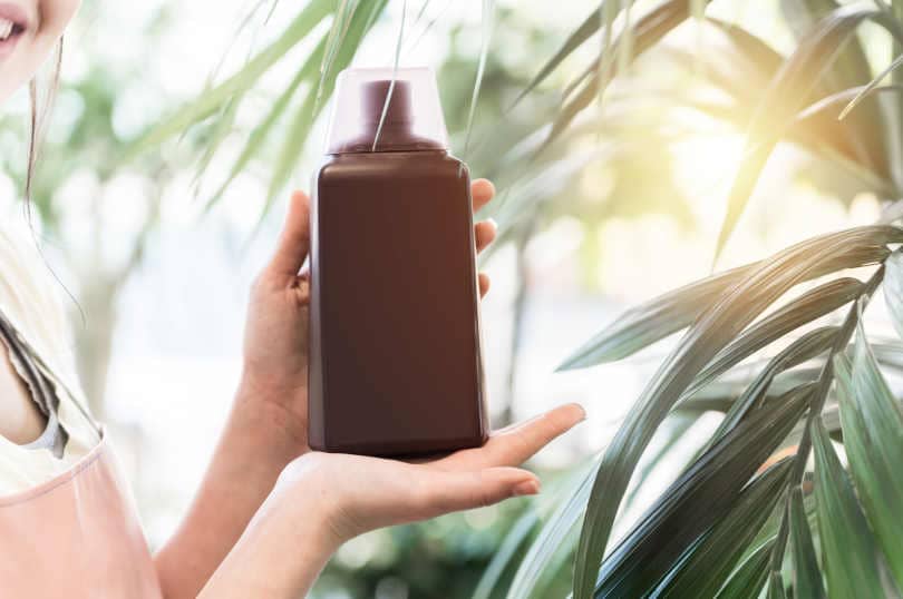 Female hands holding bottle of liquid fertilizer in garden