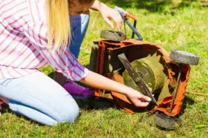 Gardener mowing green lawn with lawnmower, checking mower blade