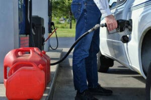 Man pumping gas into the gas tank of his vehicle car truck with gas cans lined up ready to be filled