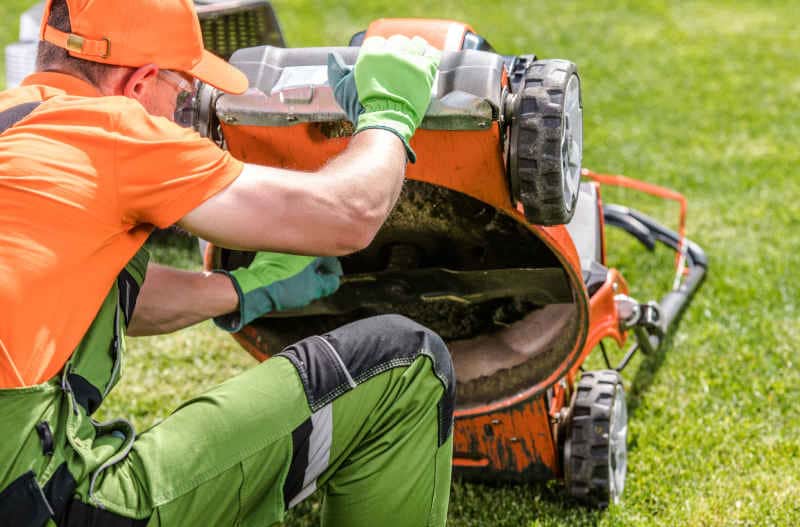 Professional Caucasian Landscaper Checking on Lawn Mower Blade While Cutting Backyard Garden Grass Field.
