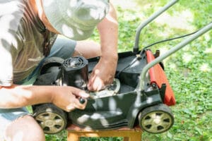 A man repairs a lawn mower in the backyard of the house